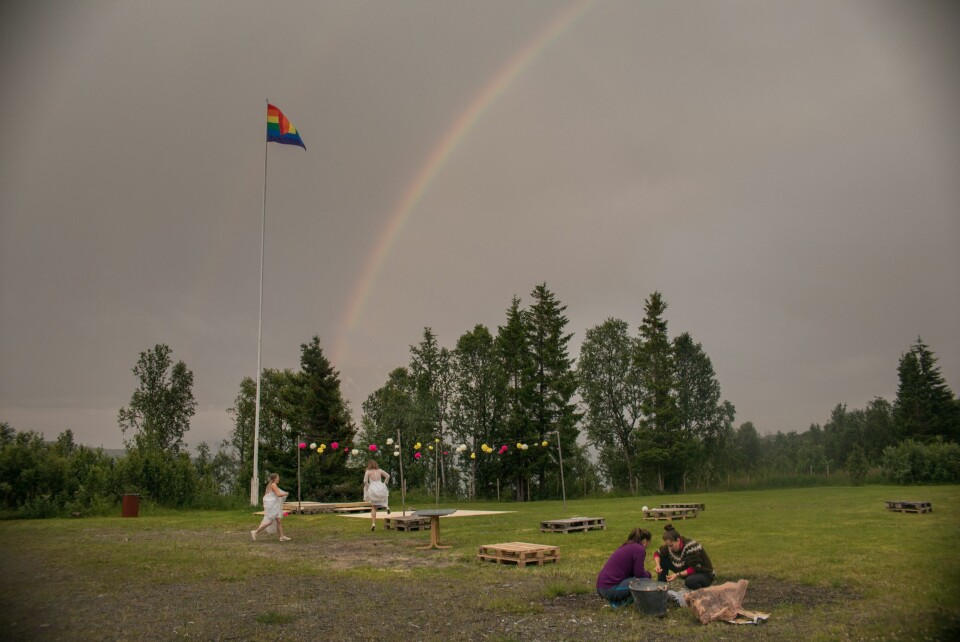 Regnbueflagget vaier under en dobbel regnbue i Lyngen. Brudeparet spretter ørville rundt.