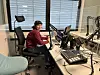 Jente som sitter og jobber forran mac og radio-utstyr