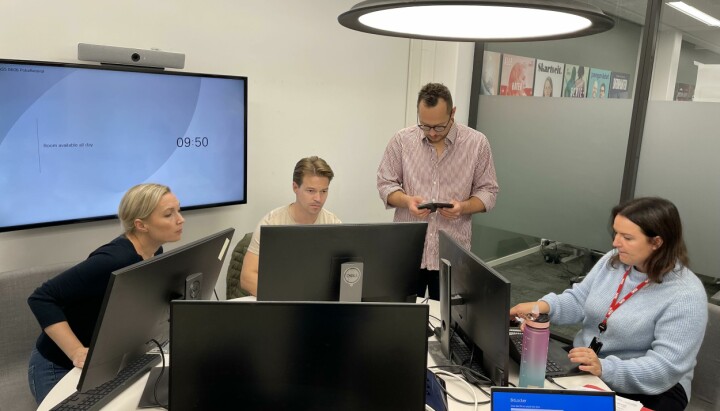 Fire journalister sitter foran dataskjermer og jobber i et grupperom