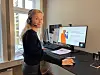 en ansatt som smiler til kamera fra arbeidspulten sin