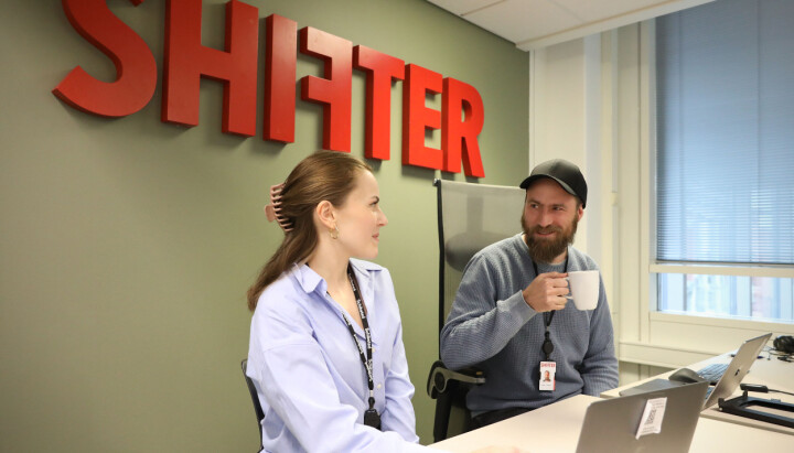To kollegaer som sitter sammen ved pulten med Shifter logo i bakgrunn