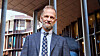 Mann i dress poserer foran et moderne kontorbygg utendørs.
