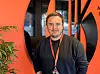 En mann med nøkkelbånd står foran en oransje vegg og svarte former i et moderne rom.