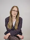 Kvinne med briller og langt hår sitter foran en lys bakgrunn.