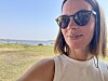 En kvinne med solbriller tar selfie ved en kystlinje med hav og gress i bakgrunnen.