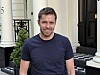 Smilende mann står foran en bygning med søyler og rutet inngangsparti.
