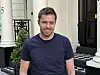 Smilende mann står foran en bygning med søyler og rutet inngangsparti.
