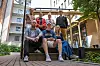 Sju personer sitter og står på en utendørs trapp ved boligblokker i et gårdsrom.