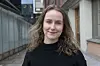 Smilende kvinne med krøllete hår fotografert utendørs mellom bygninger.
