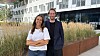 To personer står foran et moderne kontorbygg med høyt gress i plantekasser.